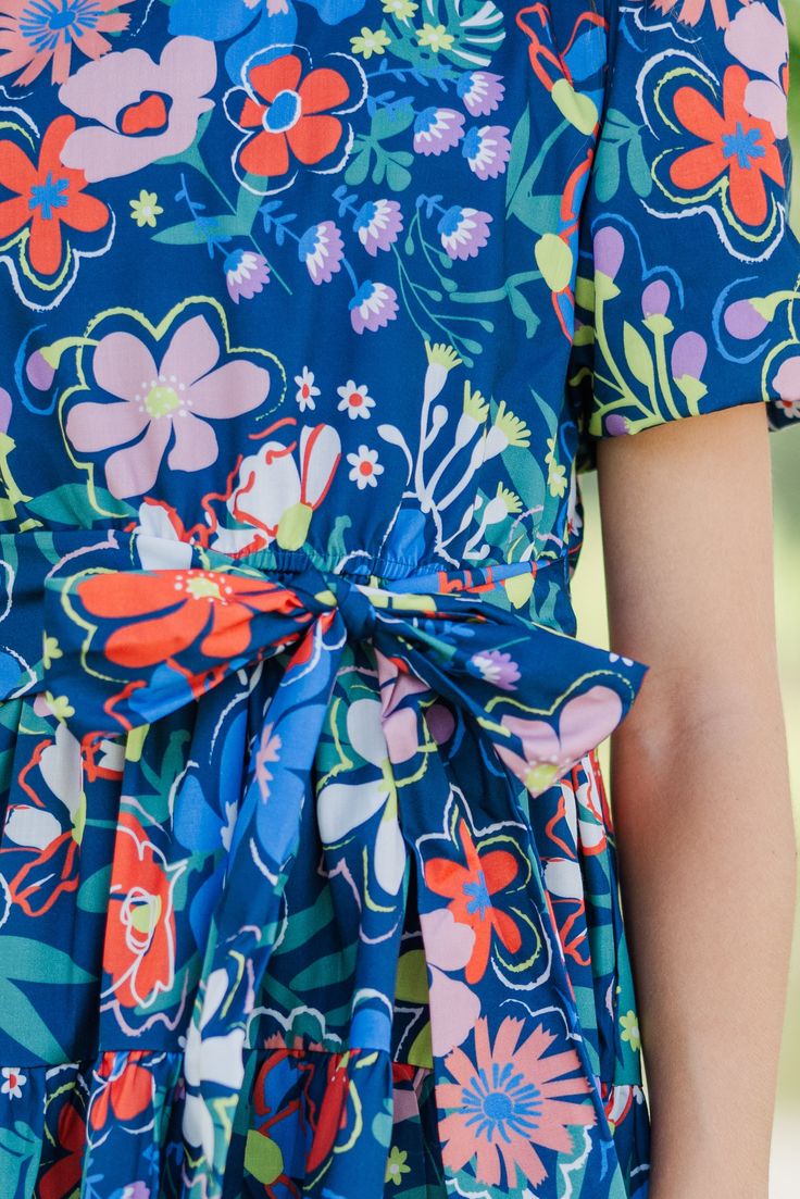 This floral dress is so bold and colorful! We just know your daughter is going to love rocking this beauty! This dress is going to be great for school, Sunday church, or any occasion where she needs to look fab! Round neckline Button keyhole back Short bubble sleeves Tied/elastic waist Floral print No stretch Morgan is wearing the small. Blue Floral Print Short Sleeve Dress, Fun Floral Print Dress For Garden Party, Fun Floral Print Dresses For Garden Party, Fun Floral Print Dress For Day Out, Fun Floral Print Dresses For Day Out, Blue Floral Short Sleeve Dress For Garden Party, Blue Printed Floral Dress For Garden Party, Blue Printed Floral Dress For A Day Out, Blue Floral Dress For Day Out