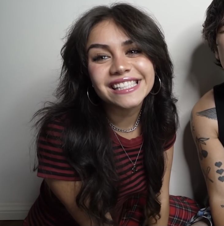 two people sitting next to each other with tattoos on their arms and chest, one smiling at the camera