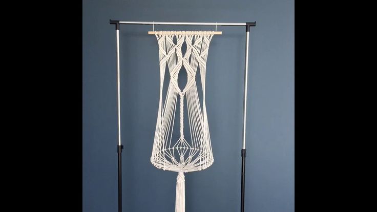 a white macrame hanging from a black pole on a blue wall in front of a gray wall