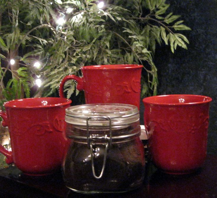 three red mugs sitting on top of a table next to a potted plant