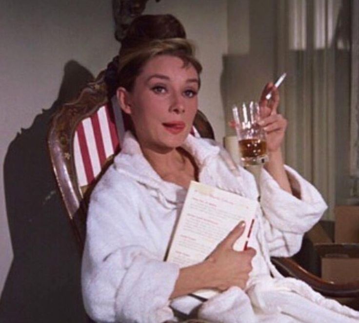 a woman in a bathrobe holding up a glass of wine while sitting on a chair