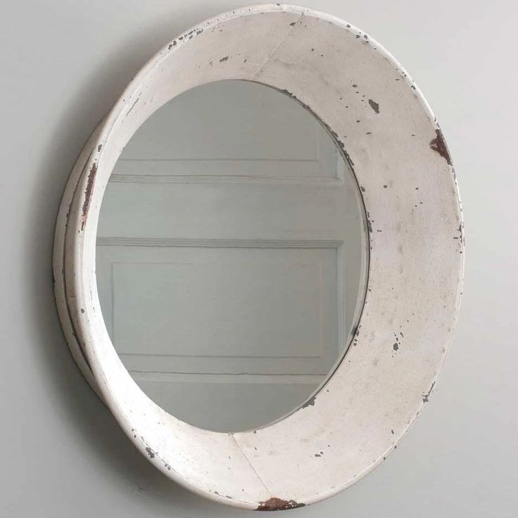 a round mirror hanging on the wall next to a white door with peeling paint over it