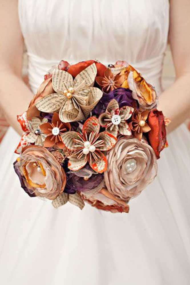 a bridal holding a bouquet of flowers made out of old book pages and brooches