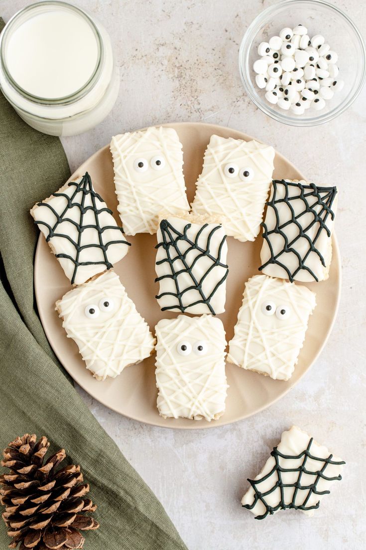 white frosted cookies decorated with spider webs and eyes on a plate next to a glass of milk