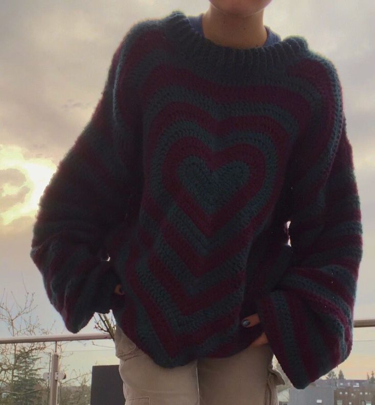 a woman standing on top of a roof wearing a sweater with a heart in the middle