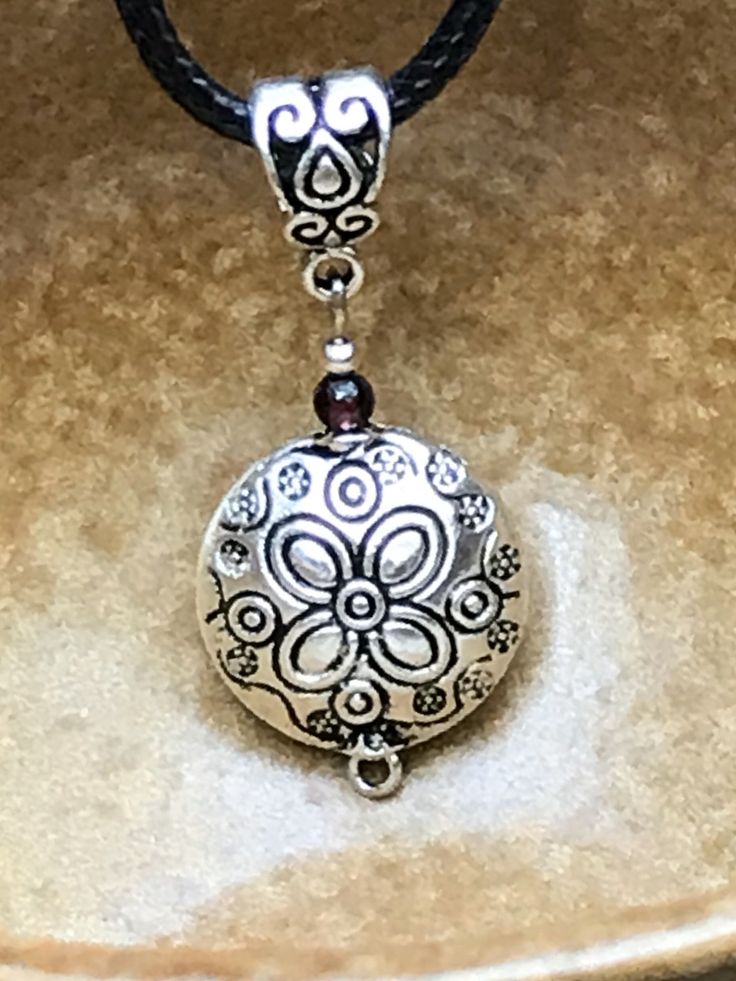 "Boho silver and garnet flower pendant necklace. This pendant necklace is so chic and unique! It has incredible detail and is very versatile. Dress it up or down! Definitely a go to necklace that you will wear often. The pendant measures 1. 25\" tall by 5/8\" wide and is made from allergy free plated silver with a small Garnet gemstone. The engraved flower patterns really adds to the beauty of this simple yet elegant pendant necklace. All my jewelry comes gift boxed with a custom Shelly Mariposa Silver Necklace With Detachable Flower Pendant, Silver Necklace With Flower Charm Oval Pendant, Silver Necklaces With Flower Charm And Round Pendant, Silver Necklace With Flower Charm Round Pendant, Silver Necklace With Round Flower Pendant, Bohemian Silver Flower Pendant Necklace, Silver Medallion Necklace With Flower Charm, Silver Amulet Necklace With Flower Pendant, Silver Boho Necklace