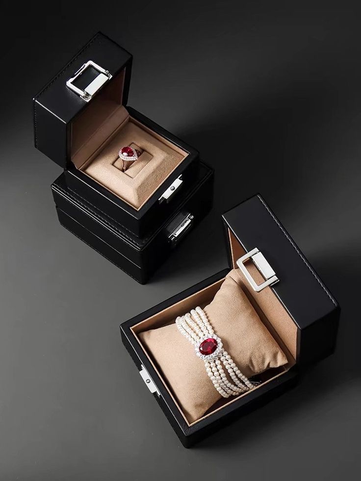 two black boxes with rings and pearls in them