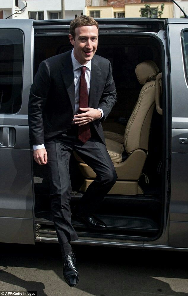 a man in a suit and tie stepping out of a silver van with the door open