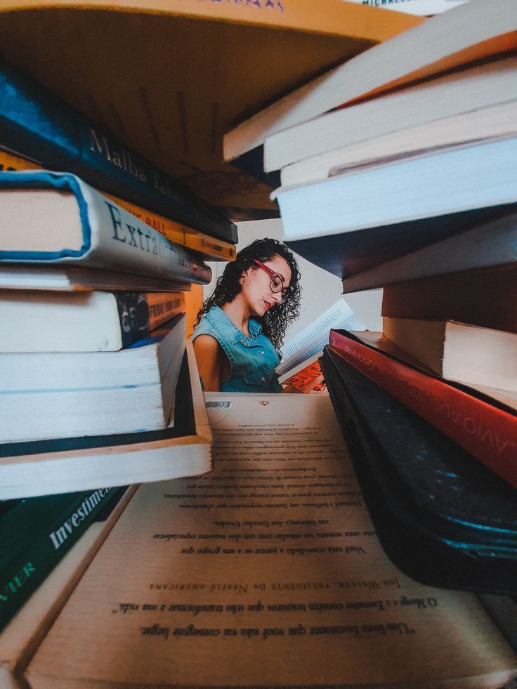 a woman is sitting in a box with books on top of her and looking at the camera