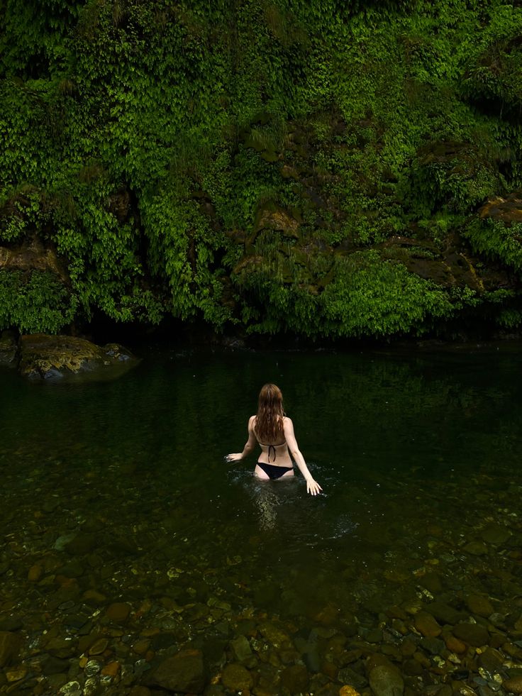 a woman sitting in the middle of a body of water surrounded by lush green trees