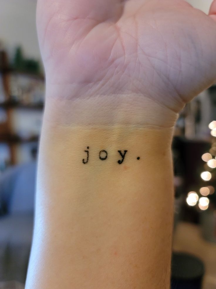 a woman's wrist with the word joy written in small black ink on it