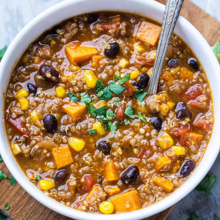 a white bowl filled with chili and sweet potato soup on top of a wooden cutting board