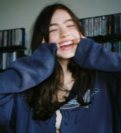 a woman is smiling and covering her face with a blue jacket in front of bookshelves