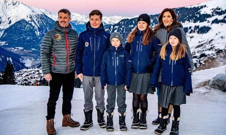 a group of people standing on top of a snow covered slope with mountains in the background