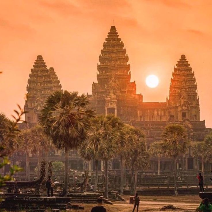 the sun is setting in front of an ancient building with palm trees and people walking around