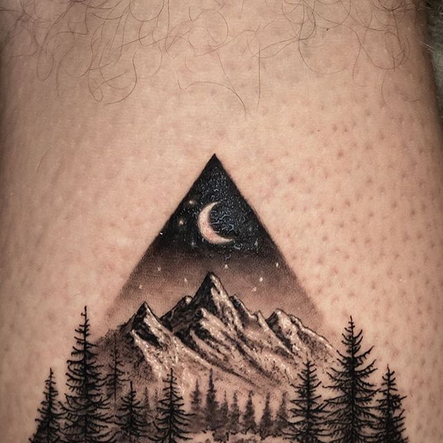 a man's thigh with a mountain and pine trees on it