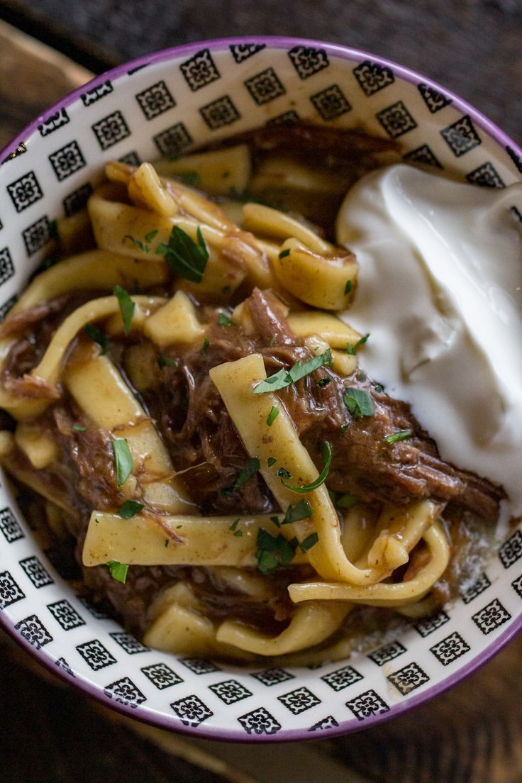 a bowl filled with pasta, meat and sour cream on top of a wooden table