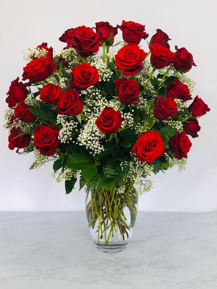 a vase filled with red roses and white baby's breath on a marble surface