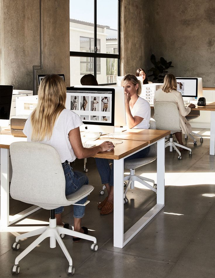 two women sitting at desks in an office with multiple monitors and laptops on them