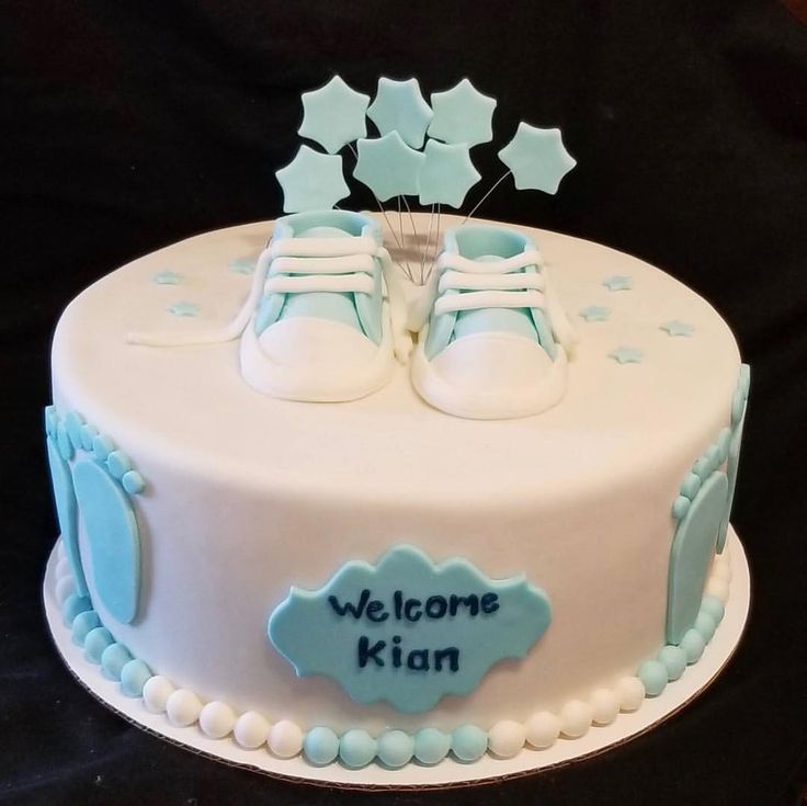 a white cake with blue icing and baby shoes on top that says welcome kian