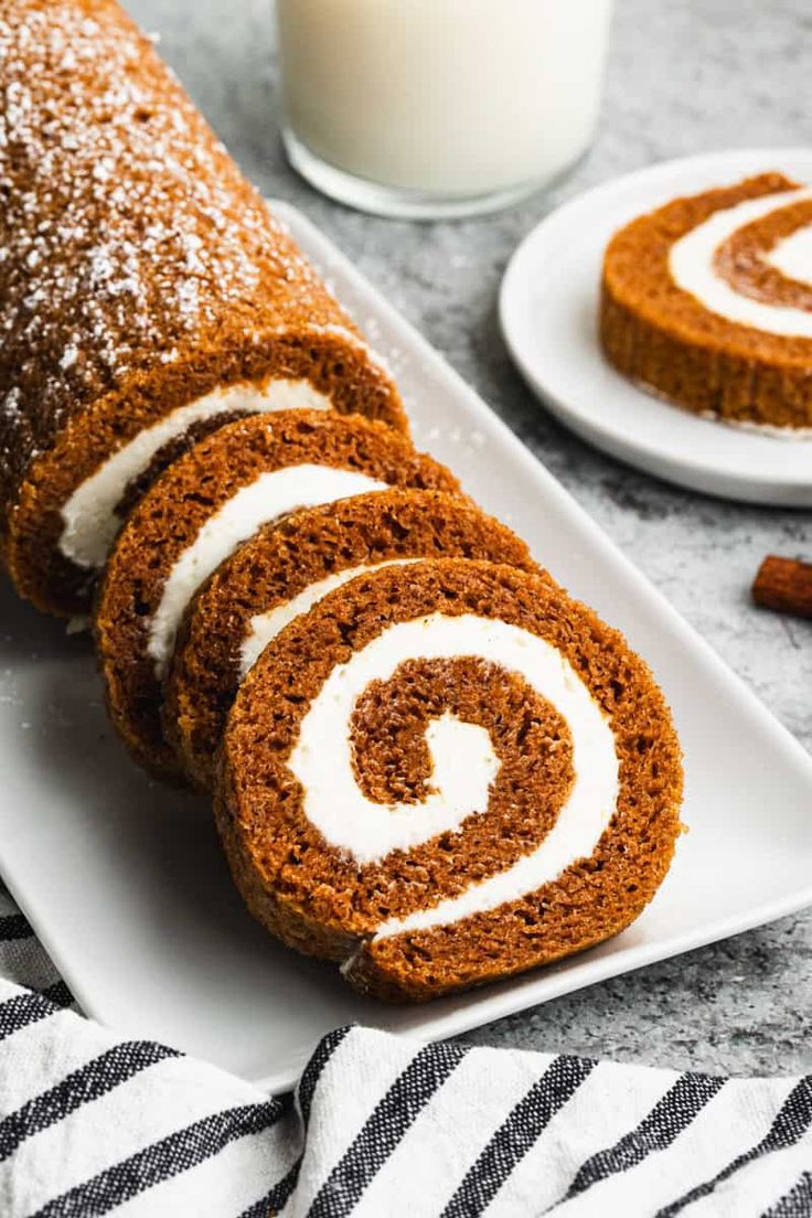 cinnamon roll on a white plate next to a glass of milk and some cinnamon sticks