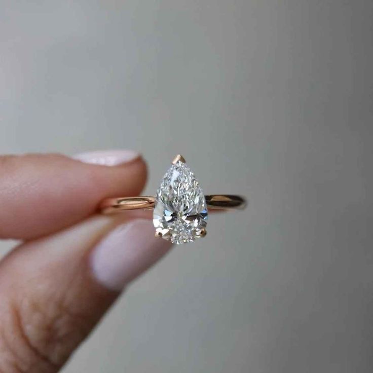 a woman's hand holding an engagement ring with a pear shaped diamond