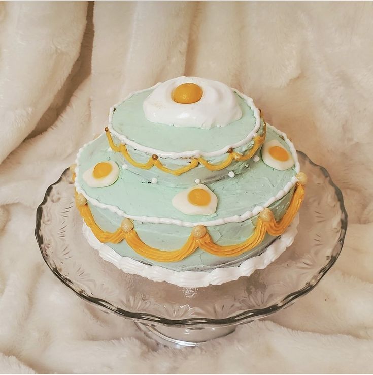 a three tiered cake with eggs on top is sitting on a glass platter