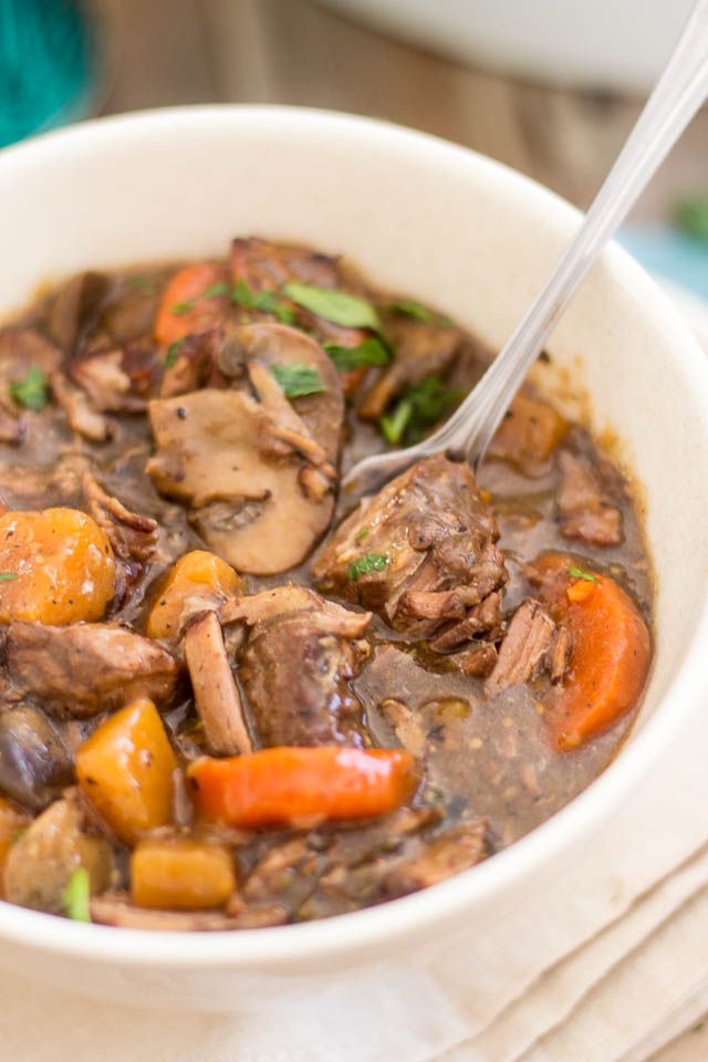 a white bowl filled with beef stew and carrots on top of a napkin next to a spoon