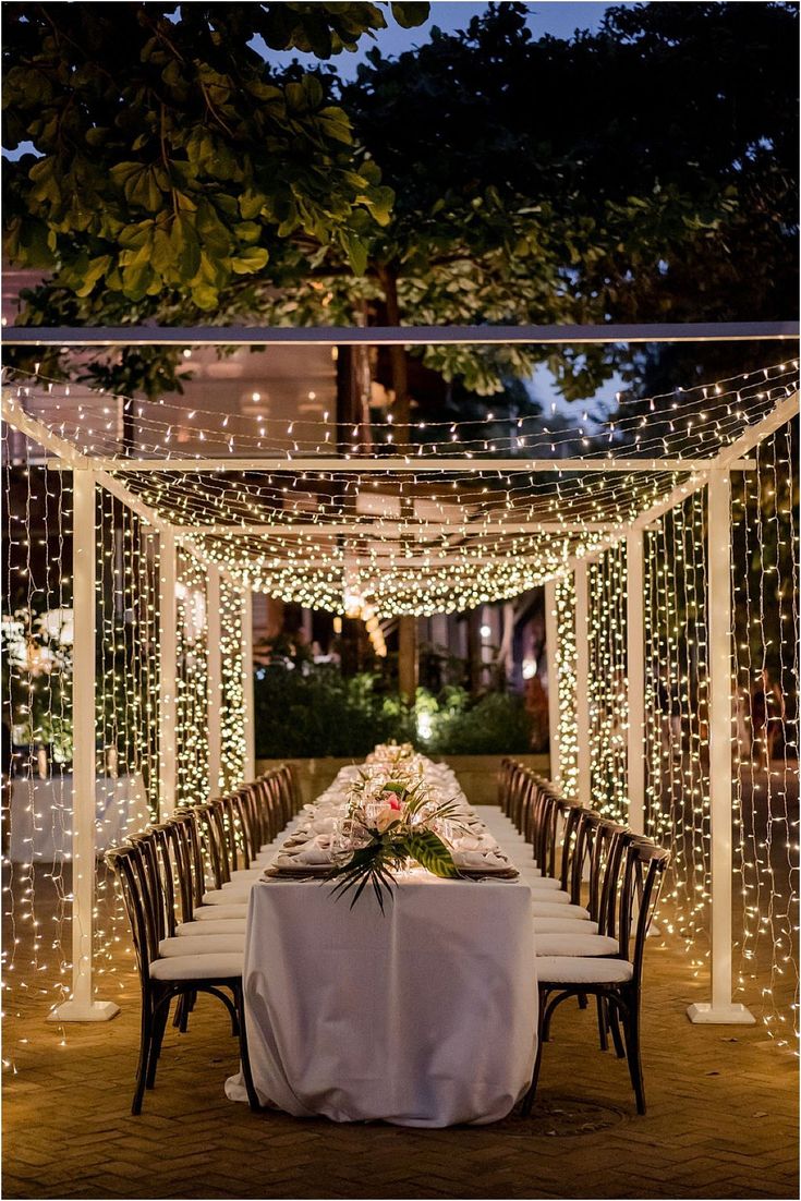 a long table with white linens and string lights is set up for an outdoor dinner