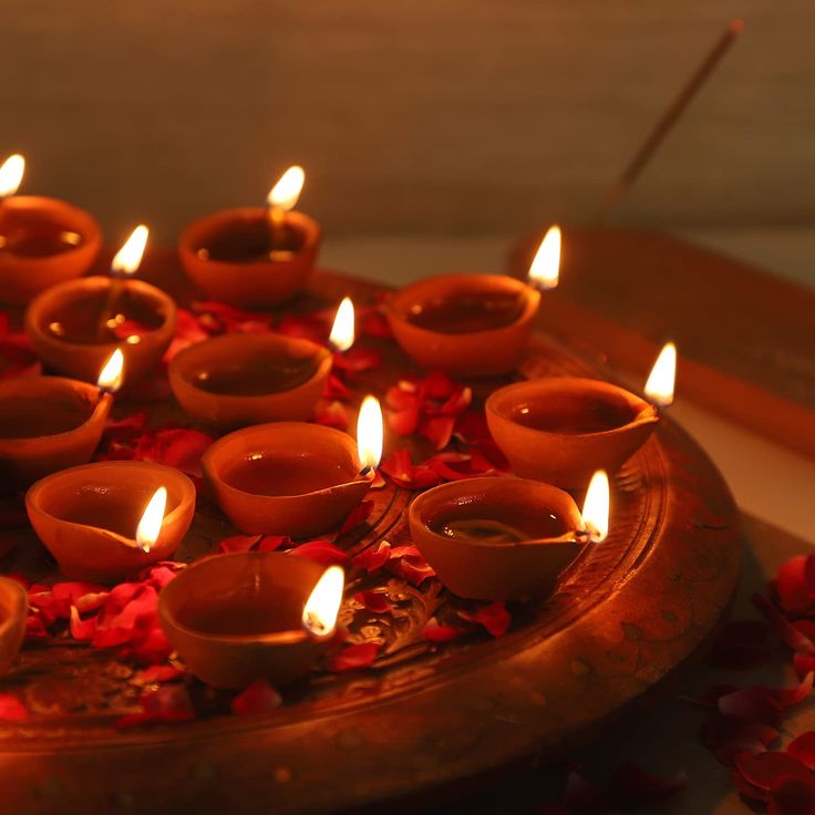 many lit candles are placed on a tray with rose petals around it and one candle is in the middle