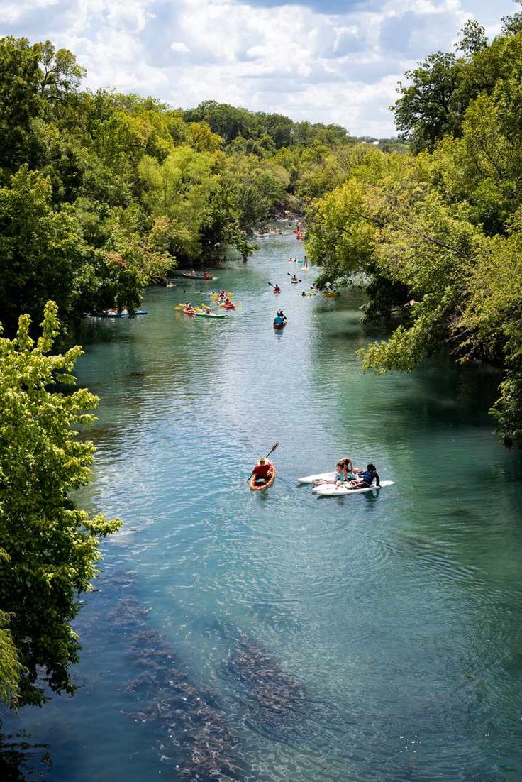 several people in canoes paddling down a river surrounded by green trees and blue water