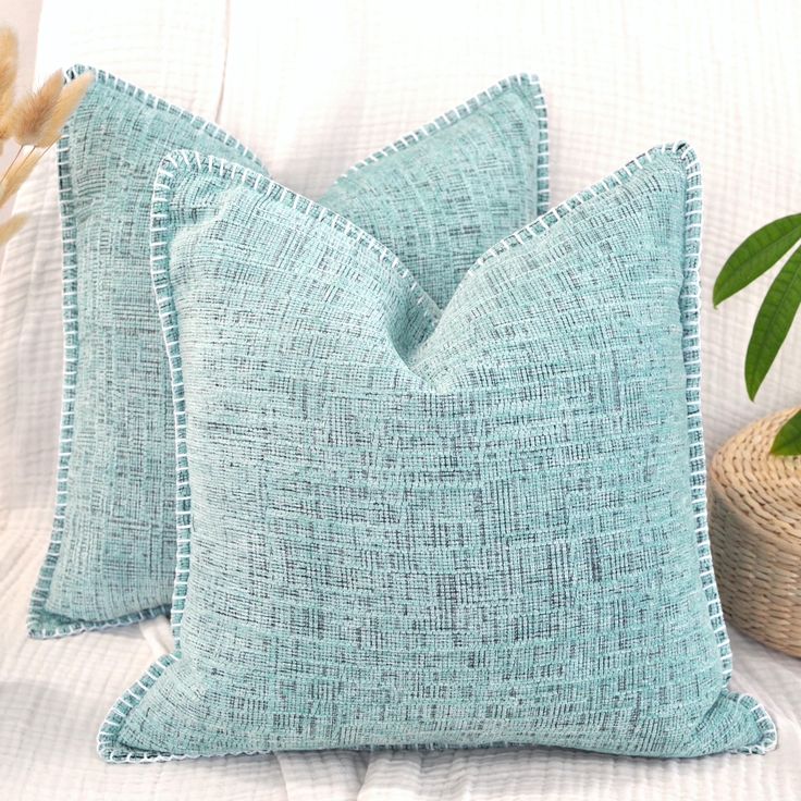 two blue pillows sitting on top of a bed next to a basket with plants in it