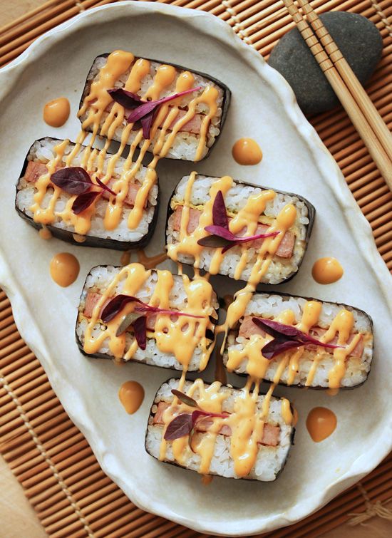 sushi with cheese and sauce on a plate next to chopsticks in a bowl