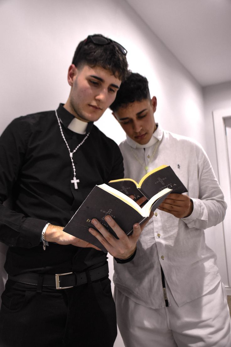 two young men standing next to each other while looking at a book