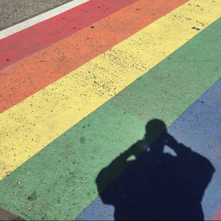 the shadow of a person standing in front of a rainbow painted street with a skateboard