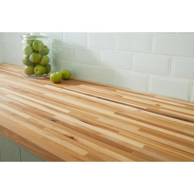 a jar filled with green apples sitting on top of a wooden counter next to a wall