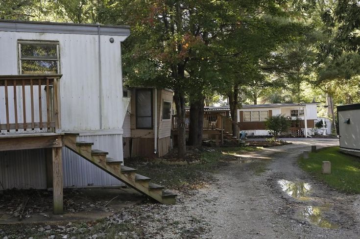 an old mobile home sits on the side of a dirt road next to some trees