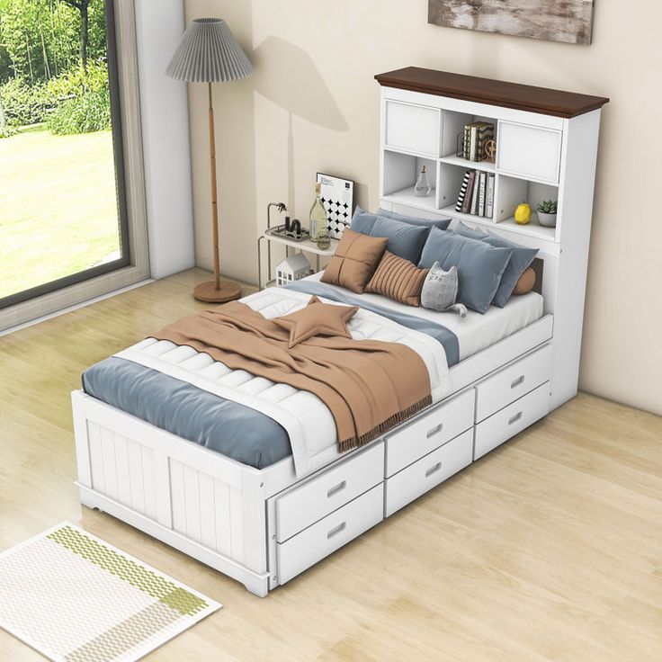 a bedroom with a bed, bookcases and drawers on the floor in front of a large window