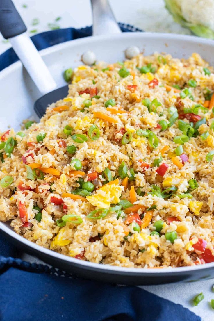 a pan filled with rice and vegetables sitting on top of a blue towel next to a fork