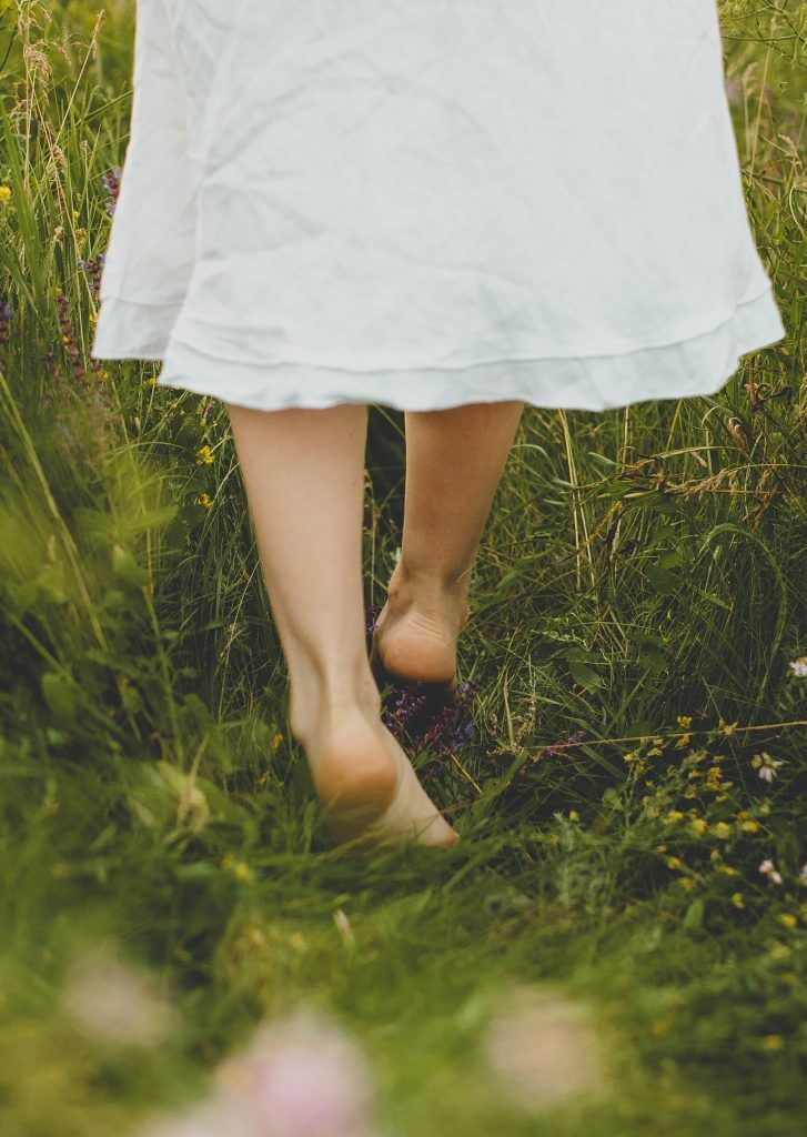 a woman walking through the grass with her bare feet in the air and wearing a white dress