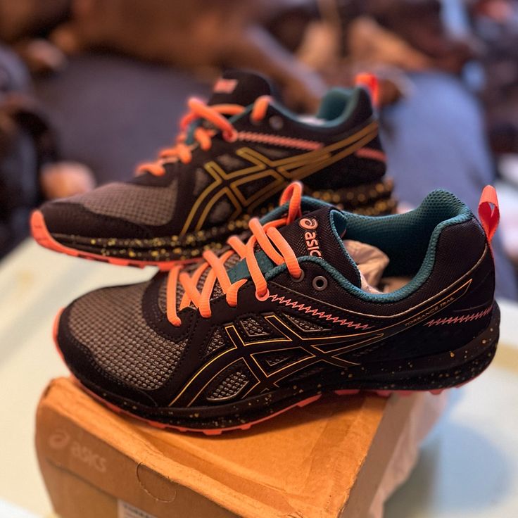 two black and orange running shoes sitting on top of a wooden box in a store