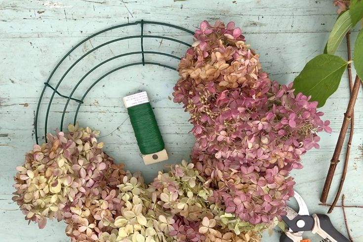 some scissors and flowers on a white wooden table with a green spool, wire