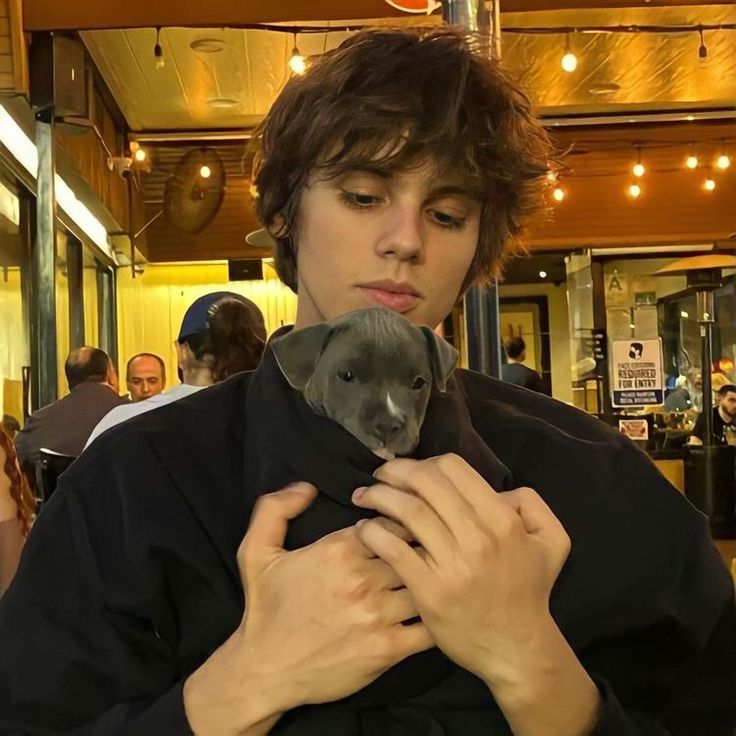 a young man holding a small animal in his hands at an indoor venue with people looking on