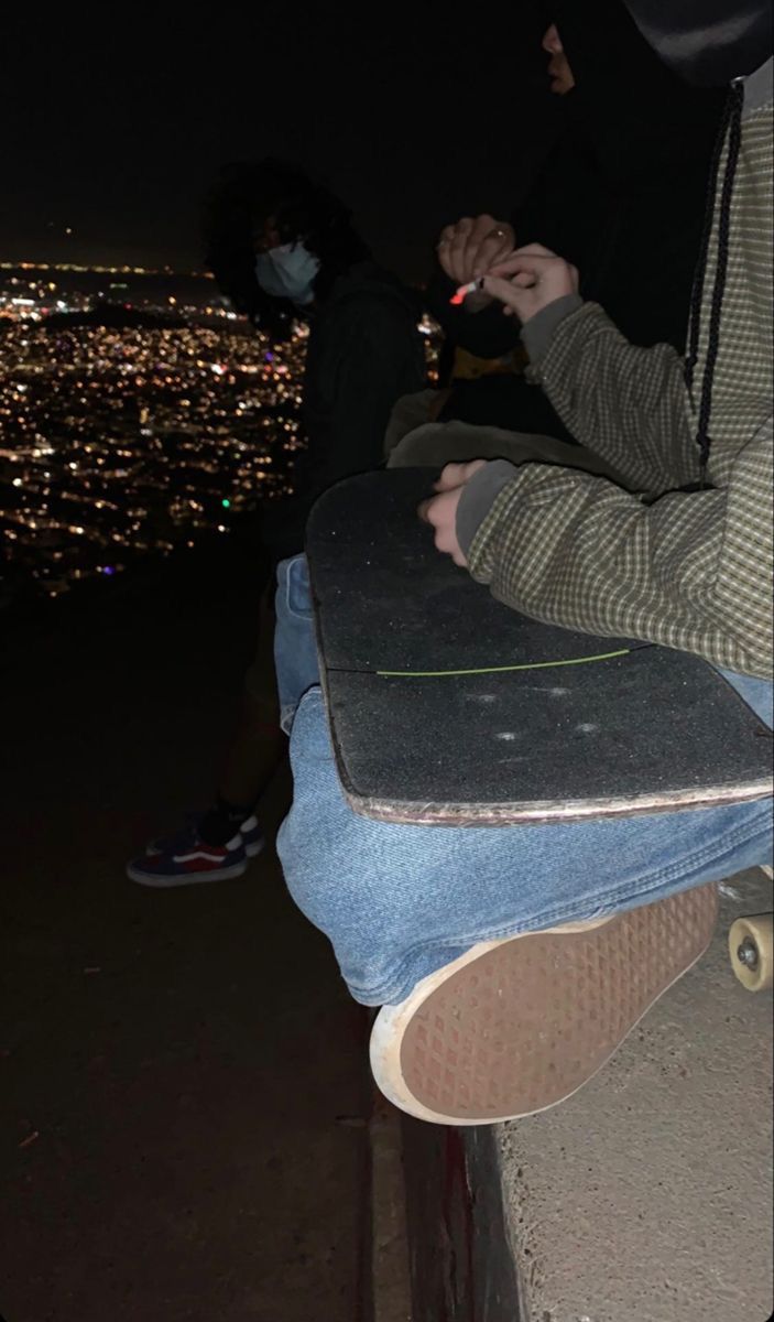 two people sitting on top of a building at night with their skateboards in front of them