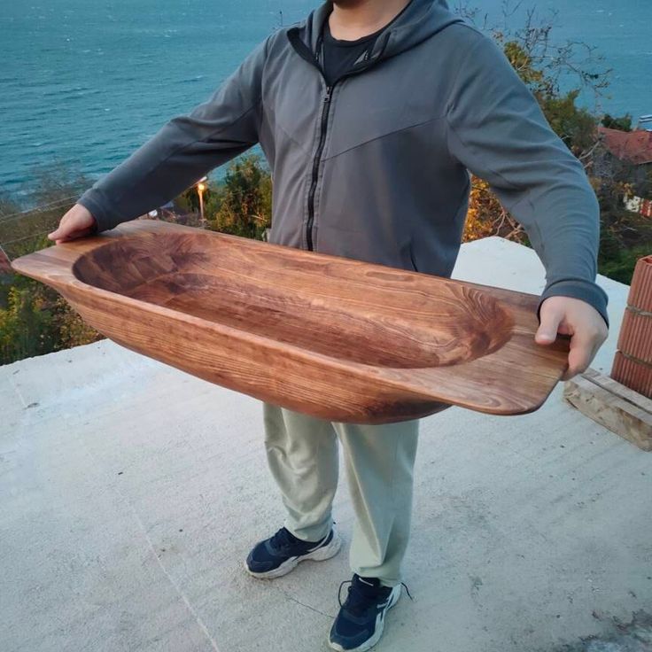 a man holding a wooden surfboard on top of a cement floor next to the ocean