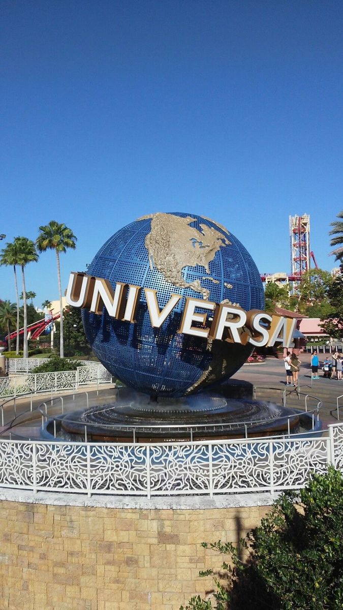 a large blue globe with the word universal on it in front of a brick wall and palm trees