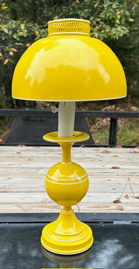 a yellow table lamp sitting on top of a wooden deck in front of trees and bushes