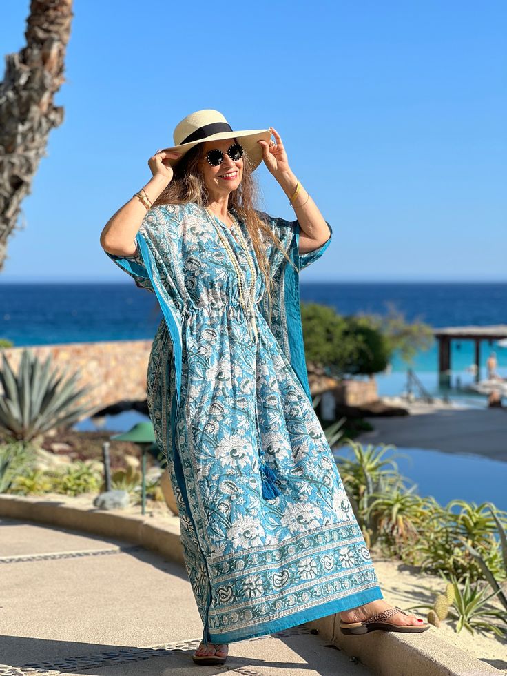 Our Aegean Blue Floral Maxi is an all over floral kaftan dress that is the perfect piece to dress up and wear out, wear to the beach as a cover-up, or just lounge about in it at home! This beautiful dress is named after none other than the aegean blue sea, which boasts the most gorgeous blue/teal colouring! Subtle variations in colour and pattern are to be celebrated as they are evidence of the hand made block printing and dyeing process that makes this dress unique. This dress is the epitome of classic comfort and is perfect to use spring, summer, and into early fall. It is also available in midi and short lengths. One size with drawstring waist Length is 54" 100% cotton voile Made in India Machine wash delicate cold in a lingerie bag to protect tassels or hand wash. Hang dry. Turquoise Maxi Dress For Beach Cover-up, Turquoise V-neck Maxi Dress For Vacation, Blue V-neck Maxi Dress For Poolside, Blue Maxi Dress For Beach Season Poolside, Blue Maxi Dress For Poolside And Beach Season, Blue Boho Dress For Beach Cover-up, Bohemian Dresses For Beach Party In Resort Season, Bohemian Beach Party Dress For Resort Season, Bohemian V-neck Maxi Dress For Resort