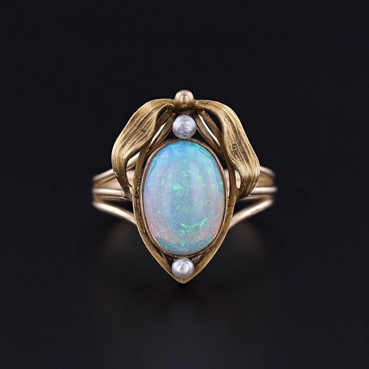 Antique Opal and Pearl Ring: This ring features a fiery white opal and two pearls mounted in 12ct gold.  The top of the ring was originally an antique stickpin (circa 1900) that our jeweler transformed by removing the pin and adding a 14k gold band. The face of the ring measures 0.8 inches by 0.6 inches wide, and it is in great condition.  The ring is a size 7, but it can be resized free of charge. Upon purchase, your ring will arrive elegantly packaged, ready for gifting or as a special treat for yourself.  We carefully wrap each piece to ensure a delightful unboxing experience. We also offer free and flexible layaway plans, so take advantage of this option to make owning your dream piece even more achievable. + Trademark Antiques Shop Homepage https://www.etsy.com/shop/TrademarkAntiques Antique Opal Ring, Bespoke Rings, Locket Charms, White Opal, Gold Band, Pearl Ring, Opal Rings, Rings Statement, Gold Bands