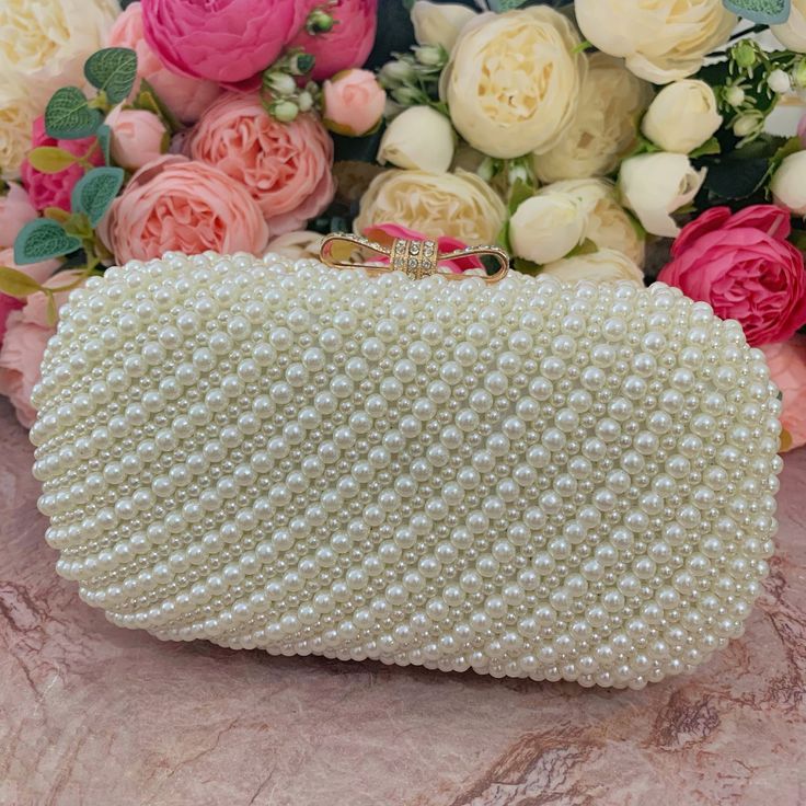 This luxurious encrusted pearl bridal clutch never fails to turn heads with its understated elegance and classic design. Adorned with varying sized ivory pearls and enhanced with a large creamy pearl clasp, this bridal clutch is the very picture of refinement. This elegant bridal clutch features rose gold trim, attachable chain and large enough for your phone. Complete your list of must-have wedding accessories with the ultimate bridal accessory to finish off your look and storing your wedding d Formal Pearl White Evening Bag, Pearl Evening Bag With Pearl Handle For Wedding Guest, Elegant Pearl White Clutch With Pearl Embroidery, Pearl Embellished Clutch, Elegant Pearl Evening Bag For Events, Cream Pearl Evening Bag For Party, Gold Pearl Evening Bag For Events, Pearl White Pearl Evening Bag For Events, Evening Pearl Embellished Bag